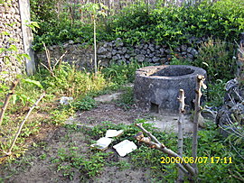 a water well sits quietly in the corner of a small plot of vegetable garden