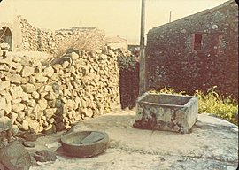 the object sitting next to the square-shaped water well looks like a stone laundry basin
			that has been sitting there unused for a long time